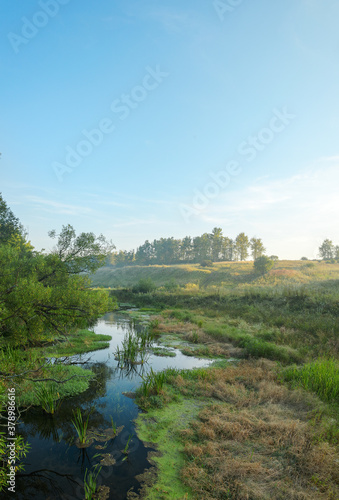 Tranquil hazy landscape with small river at sunrise
