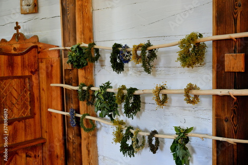 Close up on a set of flower crowns or garlands made out of heabs, vegetables and fruits hanging from three wooden poles located inside of am old Christian church to celebrate a religious event 