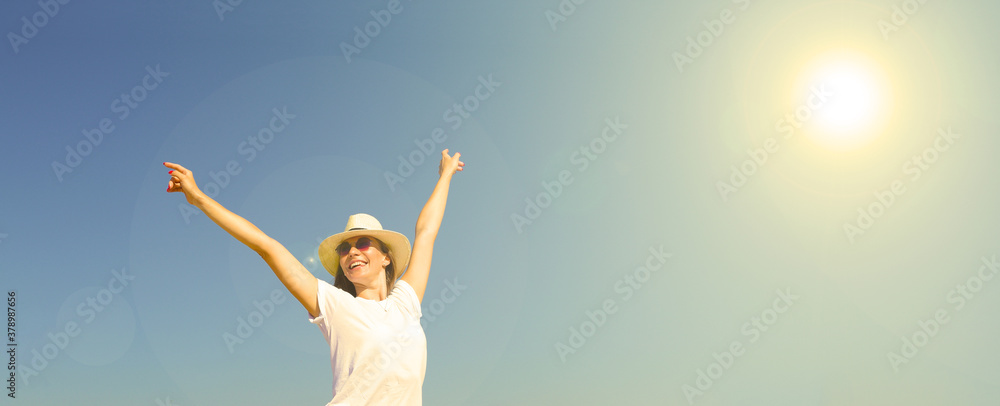 Young cheerful woman raises her hands against the blue sky. The sun is shining