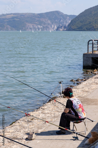 Landscape: a woman sits on the embankment of the river with fishing rods, fishing in the town