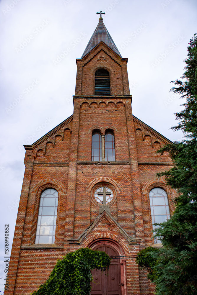 
The majestic red brick church of St. John the Baptist in the village of Opsa, Belarus. The facade of the church on a cloudy day.