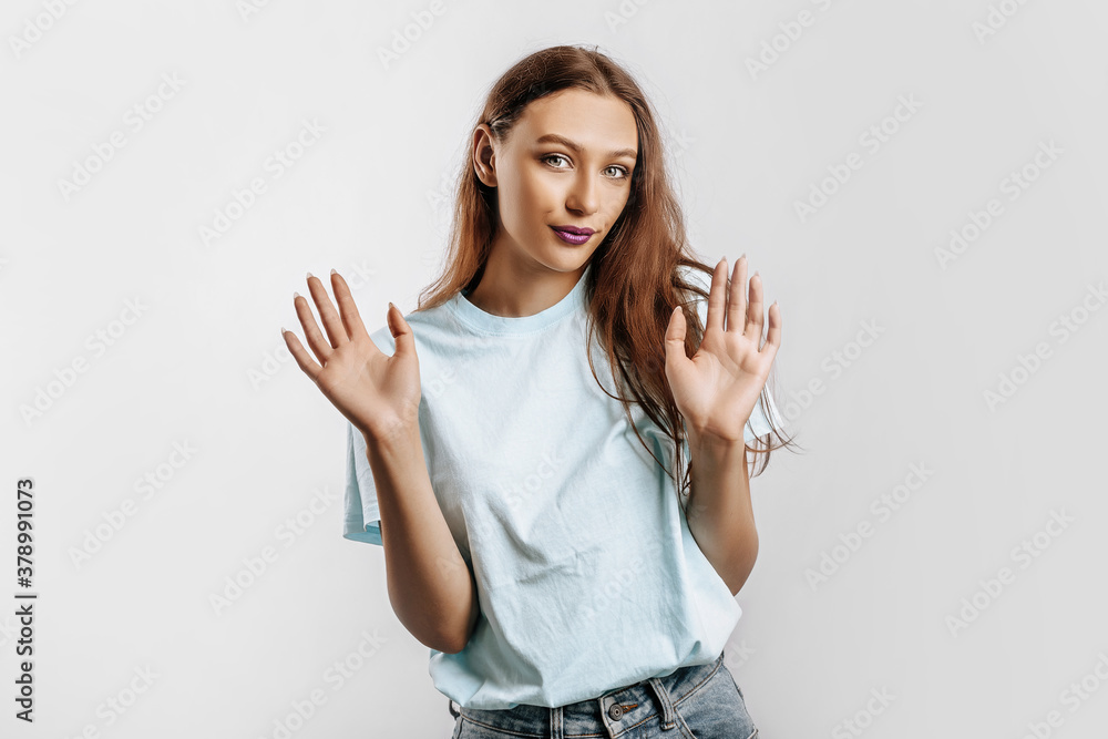 Stop. The woman raises her hands to the camera. The model feels confused and does not know what to choose. Beautiful sweet brunette girl with fashion makeup purple lips on an isolated gray background Stop. The woman raises her hands to the camera. The model feels confused and does not know what to choose. Beautiful sweet brunette girl with fashion makeup purple lips on an isolated gray background
