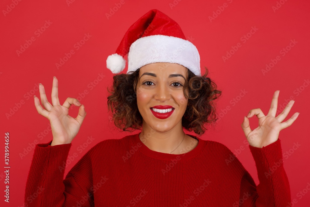 Glad attractive woman shows ok sign with both hands as expresses approval, has cheerful expression. Photo of beautiful female has appealing appearance, being optimistic. Standing against gray wall. Glad attractive woman shows ok sign with both hands as expresses approval, has cheerful expression. Photo of beautiful female has appealing appearance, being optimistic. Standing against gray wall.