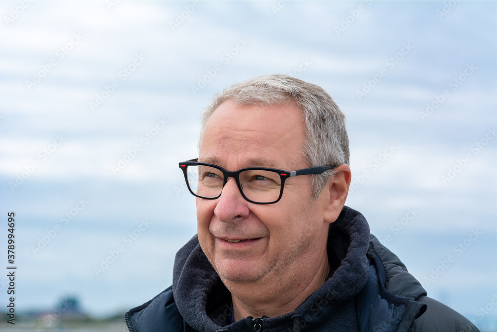 A closeup picture of a middle-aged man, in his 50s, with grey hair and glasses. Blue hazy sky in the background A closeup picture of a middle-aged man, in his 50s, with grey hair and glasses. Blue hazy sky in the background