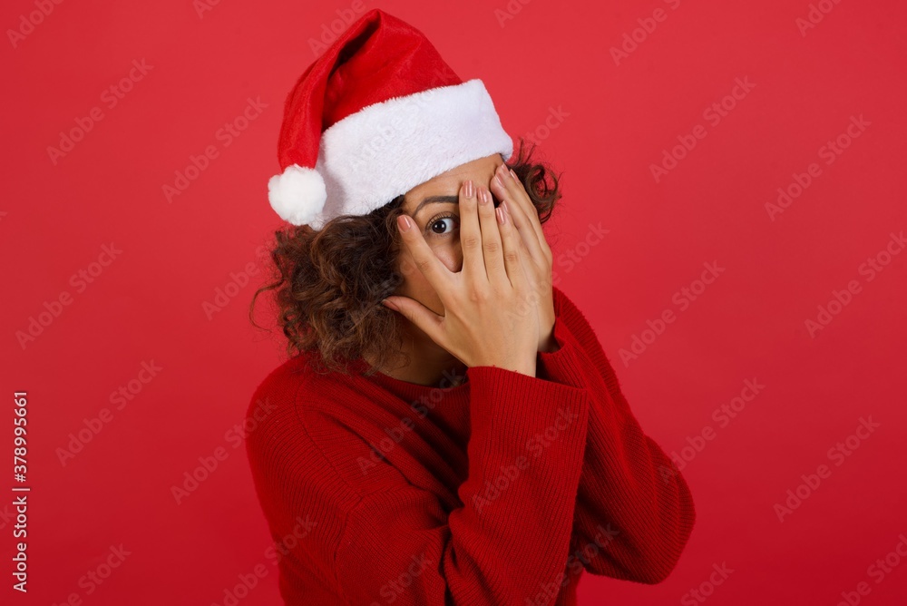 Anxiety - a conceptual image of a beautiful young caucasian woman covering her face with her hands and peering out with one eye between her fingers standing indoors. Scared from something or someone. Anxiety - a conceptual image of a beautiful young caucasian woman covering her face with her hands and peering out with one eye between her fingers standing indoors. Scared from something or someone.