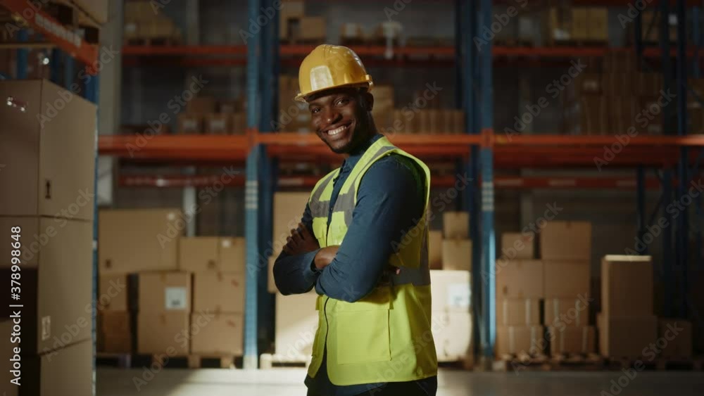 Handsome and Happy Professional Worker Wearing Safety Vest and Hard Hat Smiling and Crossing Arms on Camera. In the Background Big Warehouse with Shelves full of Delivery Goods. Medium Portrait Handsome and Happy Professional Worker Wearing Safety Vest and Hard Hat Smiling and Crossing Arms on Camera. In the Background Big Warehouse with Shelves full of Delivery Goods. Medium Portrait
