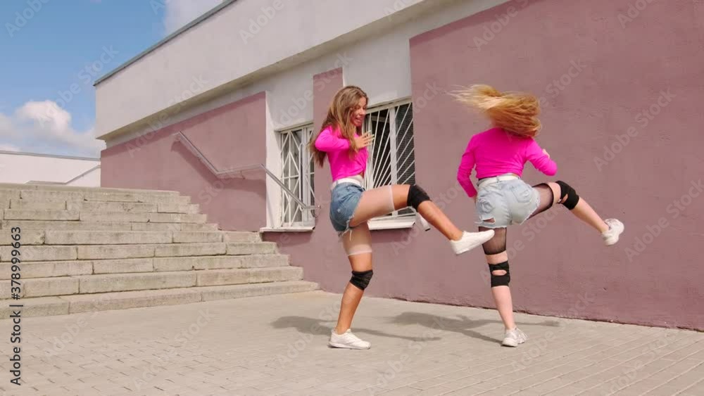 Duet of young cheerful girls in short shorts dancing free style street dancing, hip hop choreography in front of a building with a staircase. Slow motion Duet of young cheerful girls in short shorts dancing free style street dancing, hip hop choreography in front of a building with a staircase. Slow motion