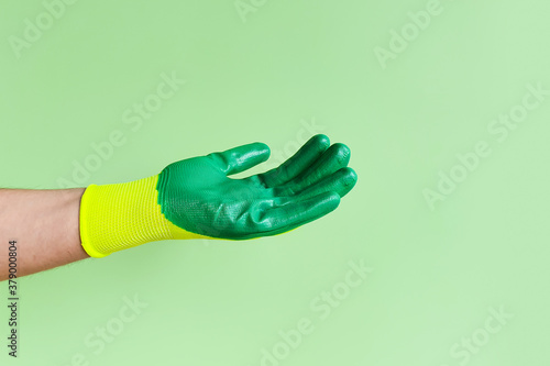 Male hand in a glove for working in the garden, vegetable garden. Worker showing outstretched palm gesture. Place for your product, Copy space. photo