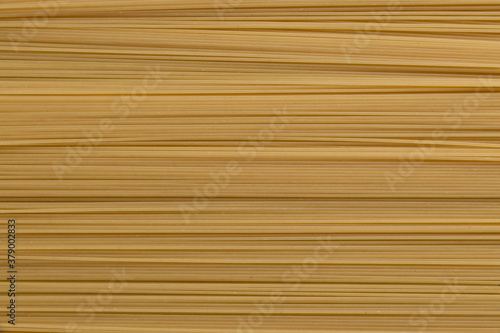 Abstract textured food background of raw uncooked spaghetti pasta made from milled durum wheat. Top down view. Copy space for your text. Italian cuisine theme.