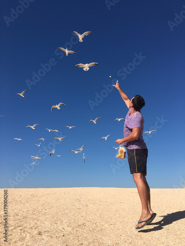 Man feeding seagulls on sandy beach against blue sky
