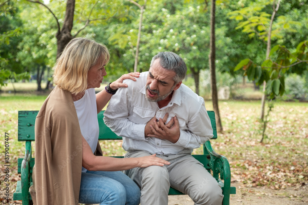 Senior male Caucasian suffering from bad hurt in his chest heart attack at park with wife care and supporting husband. Senior male Caucasian suffering from bad hurt in his chest heart attack at park with wife care and supporting husband.