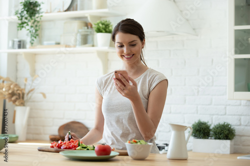 Foto Smiling young woman making salad and using mobile to count calories and plan diet