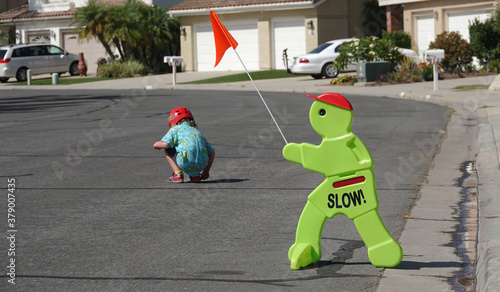 Fototapeta Naklejka Na Ścianę i Meble -  A sign urges drivers to go slow in a residential neighborhood, as a small child plays in the street.