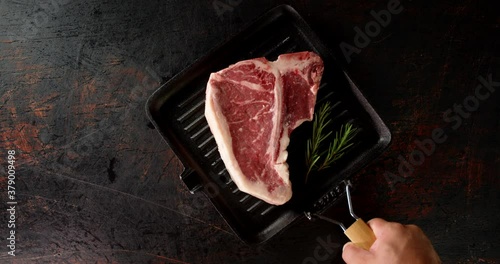 A frying pan with raw beef t-bone steak is put on table. 