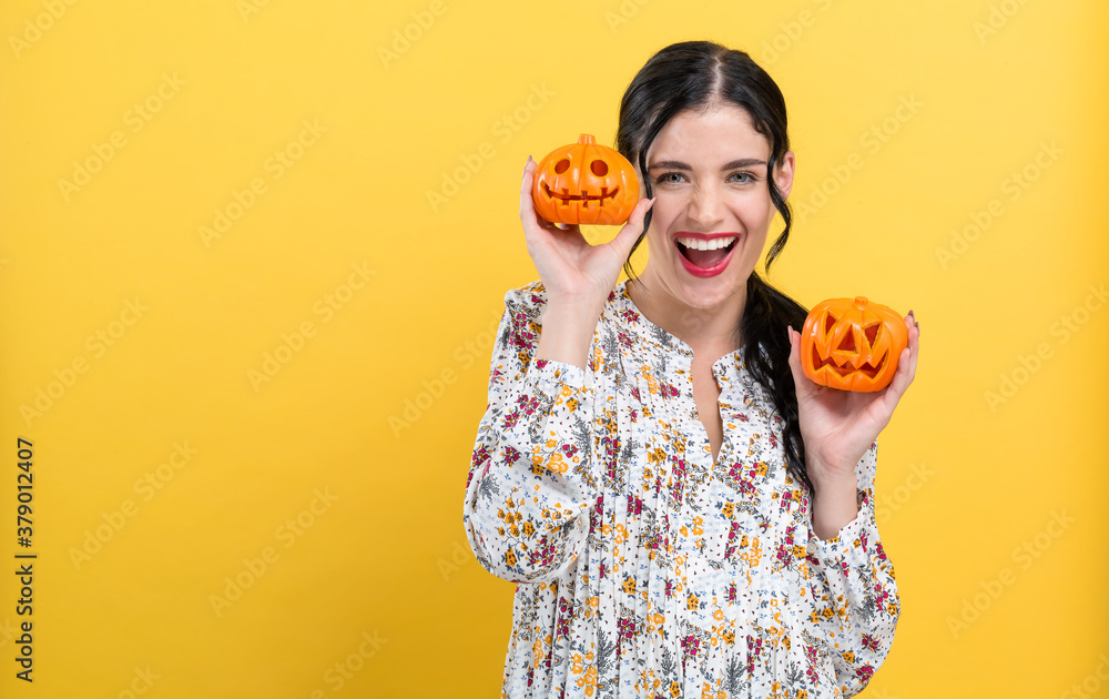 Happy young woman holding pumpkins on a yellow background