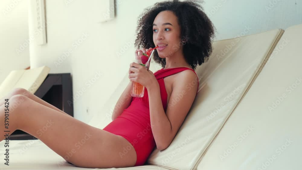 Carefree beautiful girl in red bathing suit lies in spa hotel tourist complex lounge on white couch deck chair couch, slowly drinks cold cocktail, mysteriously flirting, looks away, successful life Carefree beautiful girl in red bathing suit lies in spa hotel tourist complex lounge on white couch deck chair couch, slowly drinks cold cocktail, mysteriously flirting, looks away, successful life