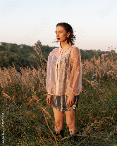 
A girl in a dress and a transparent blouse stands in the field