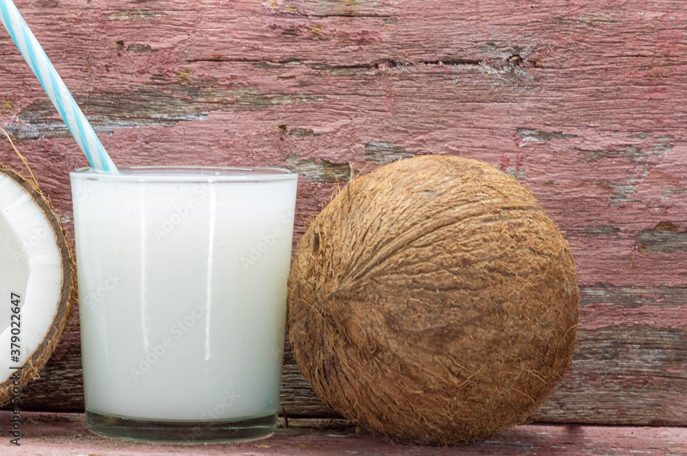 Glass of fresh coconut milk and halved fruits on aged wooden background Glass of fresh coconut milk and halved fruits on aged wooden background