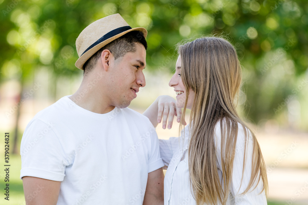 young couple looking into each other's eyes in a park. Latin man and Caucasian woman young couple looking into each other's eyes in a park. Latin man and Caucasian woman