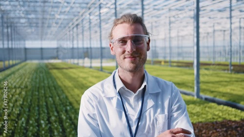 Caucasian young greenhouse worker in protective clothing standing inside modern hothouse. Portrait of successful farm engineer. Eco food. Farming business. Organics. photo