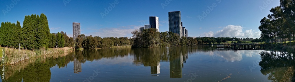 Beautiful panoramic view of a lake with reflections of luxury high-rise building, blue sky, clouds, and trees on water, lake Pavillion,  Sydney Olympic park, Sydney, New South Wales, Australia
