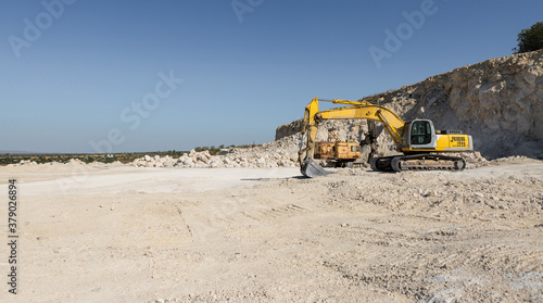 A large yellow tracked excavator is mining rock in a quarry.