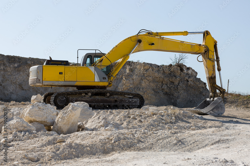 Obraz premium A large yellow tracked excavator is mining rock in a quarry.
