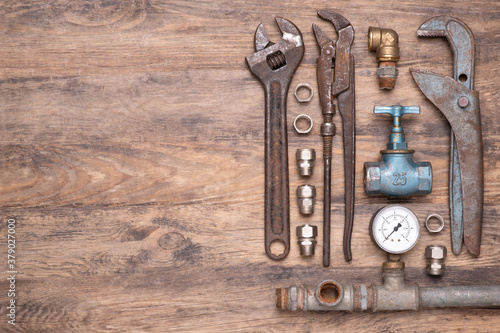 Collection of vintage plumber's tools, valves and other equipment on old wooden background, top view with copy space