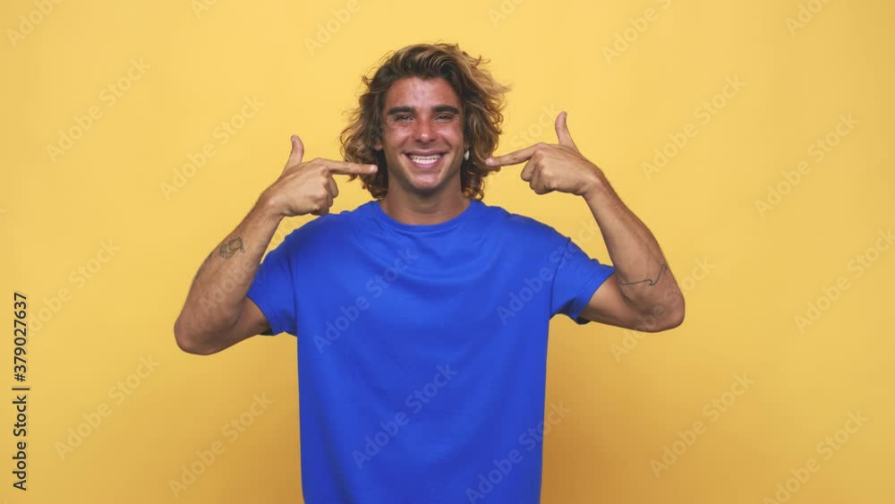 Young cool australian man smiles, pointing fingers at mouth Young cool australian man smiles, pointing fingers at mouth
