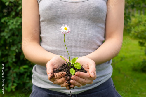 Girl carefully holds in her palms a small flower with earth in nature