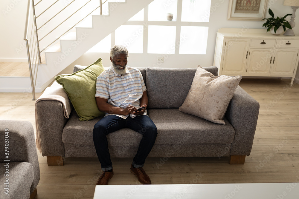 Black African American Senior man using smartphone while sitting on the couch at home Black African American Senior man using smartphone while sitting on the couch at home