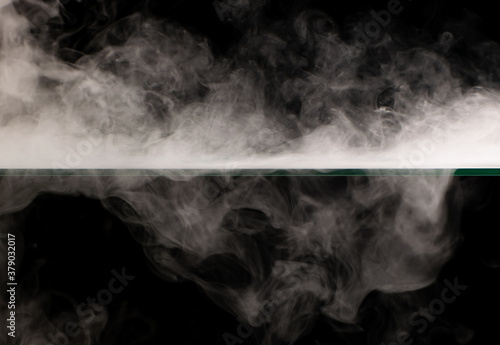 White smoke swirling spreads over the surface flowing down from the edges on a black background