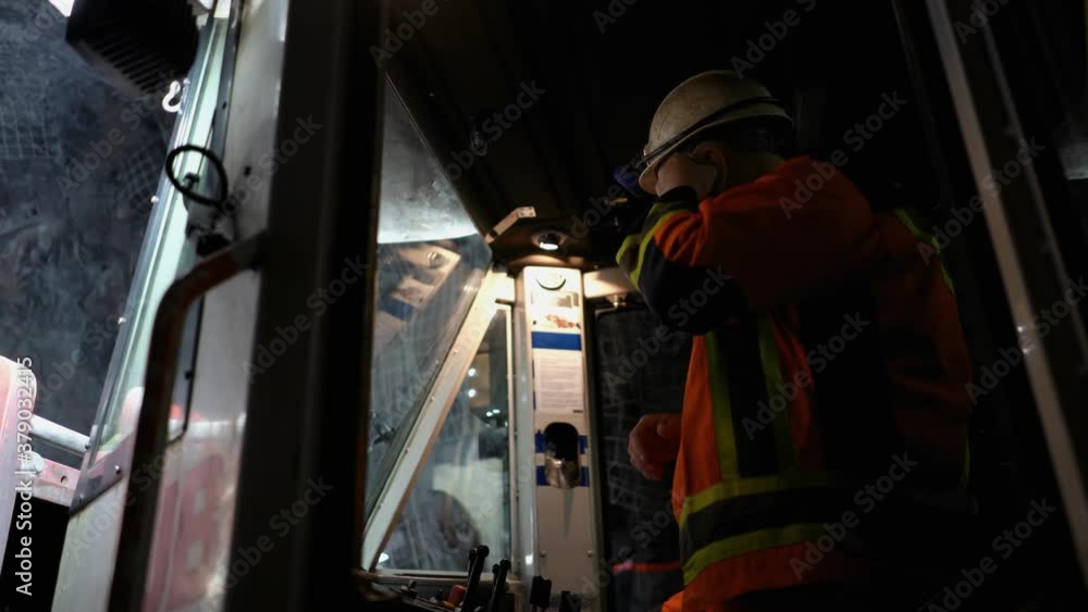 A worker in a mine wearing a hard hat and earplugs operates a drilling machine. A worker in a mine wearing a hard hat and earplugs operates a drilling machine.