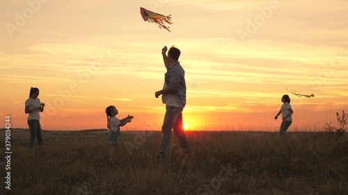 dad with children plays with kites at sunset in park. Outdoor family game. Daddy and healthy daughters are launching multi-colored paper resins into the sky. fun play with parents in sun