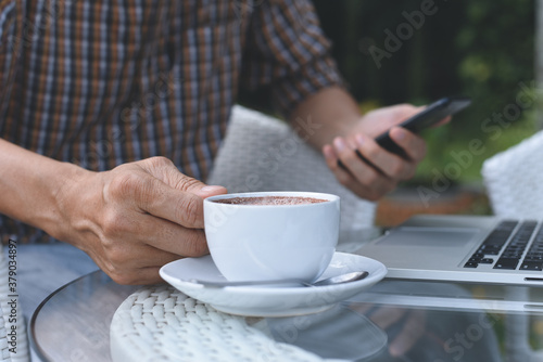 Casual man using mobile phone and drinking coffee while online working on laptop computer