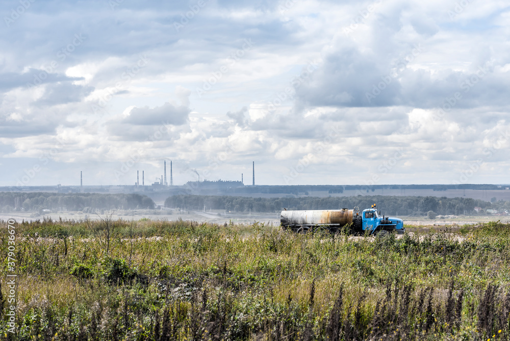 Φωτογραφία The silhouette of the plant on the horizon with smoking pipes and an old fuel tr