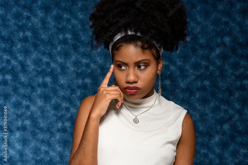 Black Afro-Brazilian teenager with his finger close to his pensive face , on a blue background Black Afro-Brazilian teenager with his finger close to his pensive face , on a blue background