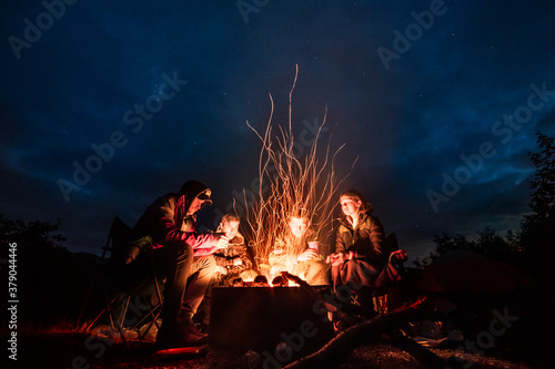 Group of friends chill and warm near a bonfire in camping during a hiking trip