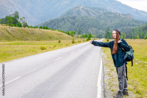 Young woman hitchhiking along a road. Empty space for text