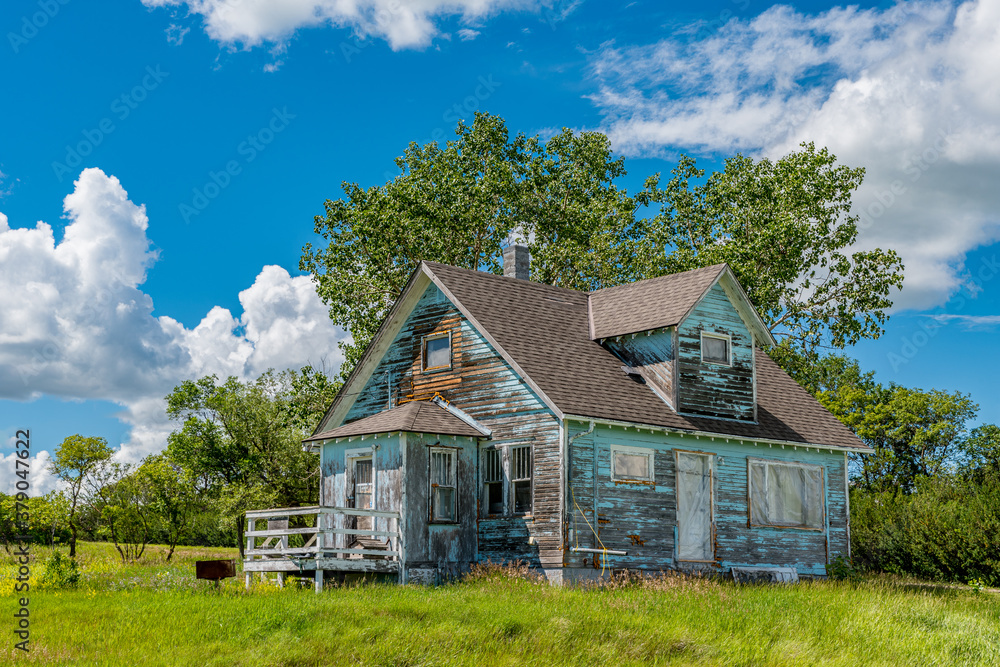Old, abandoned blue prairie farmhouse with trees, grass and blue sky in Kayville, Saskatchewan, Canada Old, abandoned blue prairie farmhouse with trees, grass and blue sky in Kayville, Saskatchewan, Canada