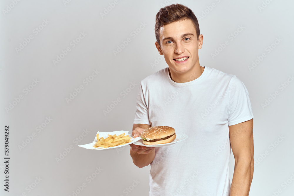 a man with fries and a hamburger on a light background in white t-shirt close-up cropped view Copy Space Model a man with fries and a hamburger on a light background in white t-shirt close-up cropped view Copy Space Model