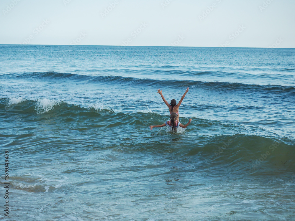 Two small children splash on the sea waves in summer, viewed from the back. Two small children splash on the sea waves in summer, viewed from the back.