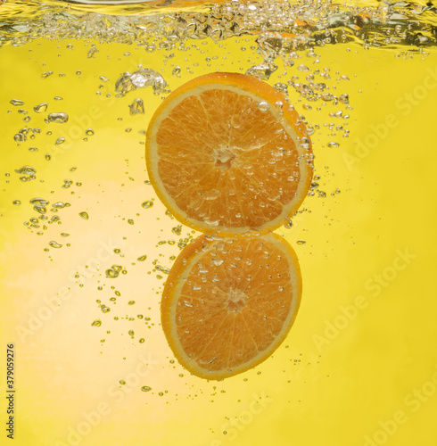 Ripe orange halves falling into water with splashes on yellow background