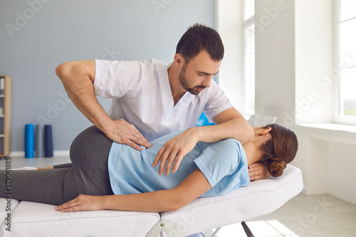 Man doctor chiropractor or osteopath fixing lying womans back in manual therapy clinic
