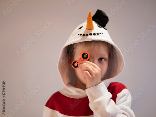 Funny blond child in nowman costume twists spiner on his nose. Portrait of boy on black background. 4K. Soothing toy. Autism. Exercise for Preschoolers photo