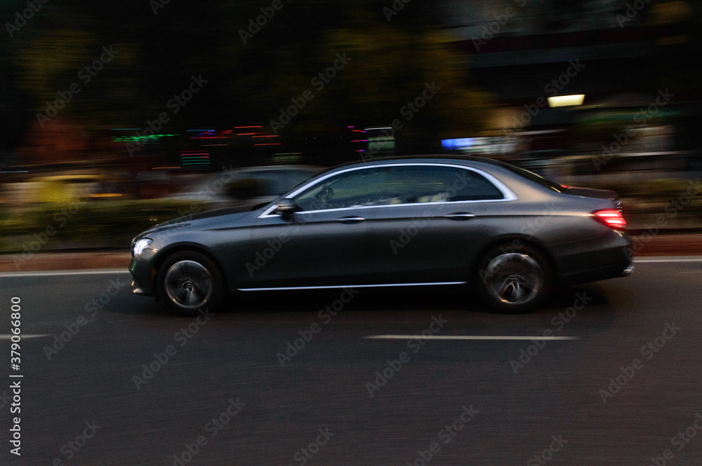 Panning technique of grey car which is going to market at night on the road