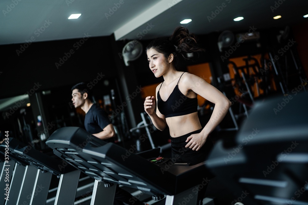 An attractive Asian woman wearing a black sportbar is exercising on a treadmill in a fitness gym.