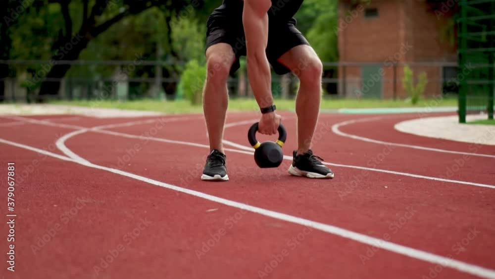A bearded man in black sportswear trains with weight bob outdoors close to the stadium on the racetrack in slowmo A bearded man in black sportswear trains with weight bob outdoors close to the stadium on the racetrack in slowmo