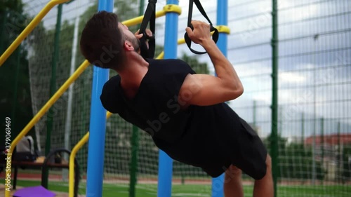 Muscular sportsman doing hanging pull ups exercise using fit belt to force strenth of workout outdoors photo