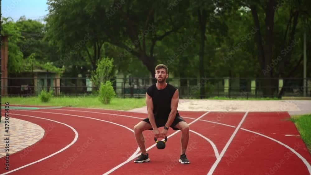 A man in black sportswear trains with weight bob outdoors close to the stadium on the racetrack A man in black sportswear trains with weight bob outdoors close to the stadium on the racetrack
